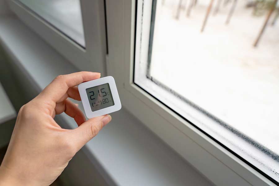 Hand som håller en hygrometer framför ett fönster med kondens